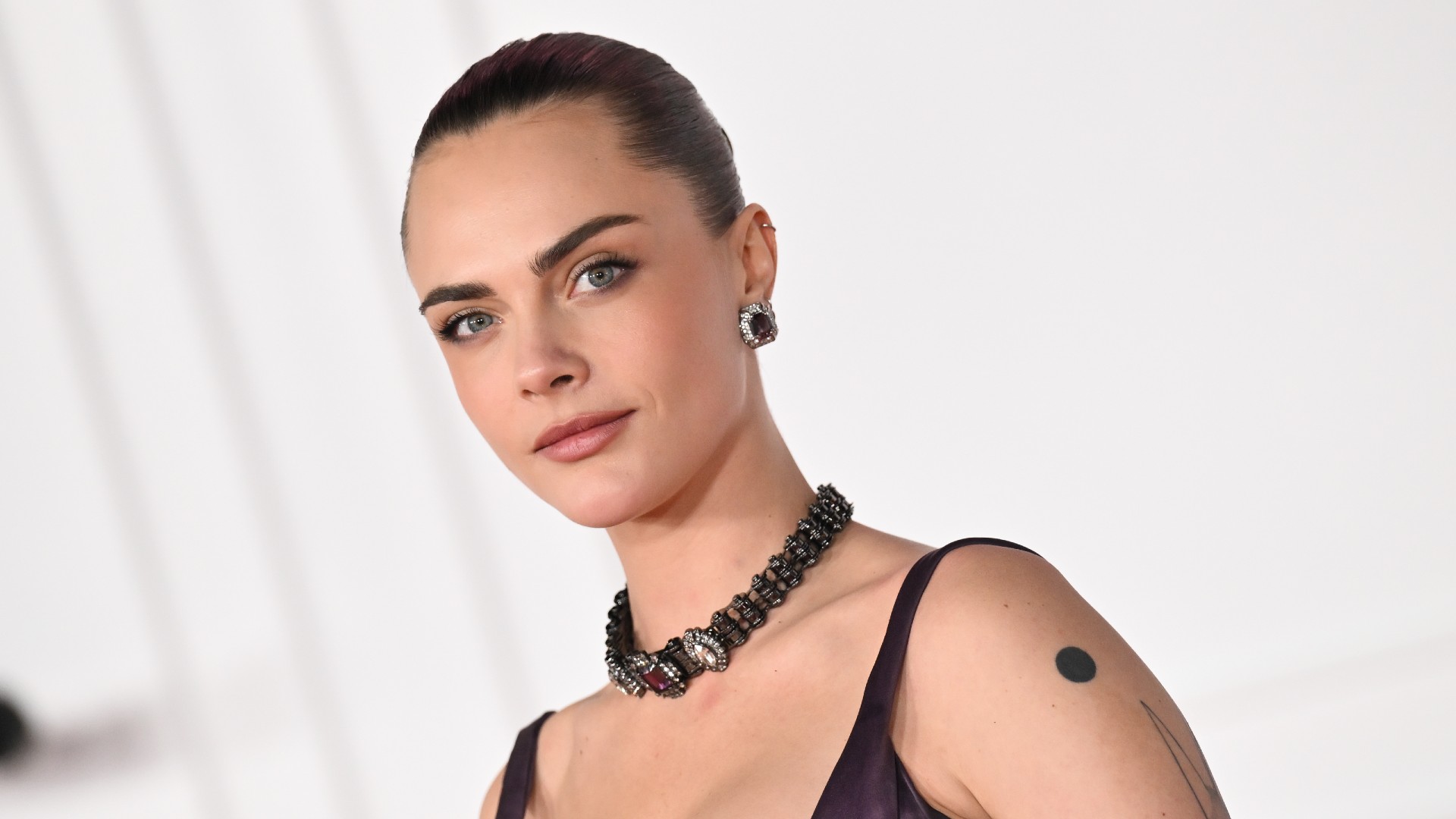 a white woman with dark hair poses for paparazzi in front of a white backdrop