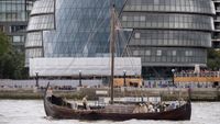 A photo of a modern replica of an actual 10th-century Viking longship on the River Thames in London. There are people on the boat and it is in front of a glass building.
