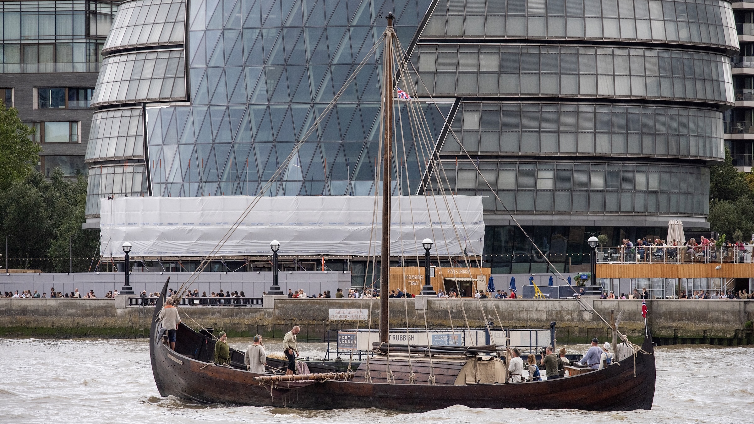 A photo of a modern replica of an actual 10th-century Viking longship on the River Thames in London. There are people on the boat and it is in front of a glass building.