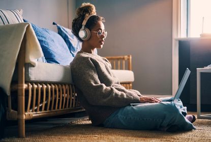 woman wearing headphones while using a laptop and sitting on the floor