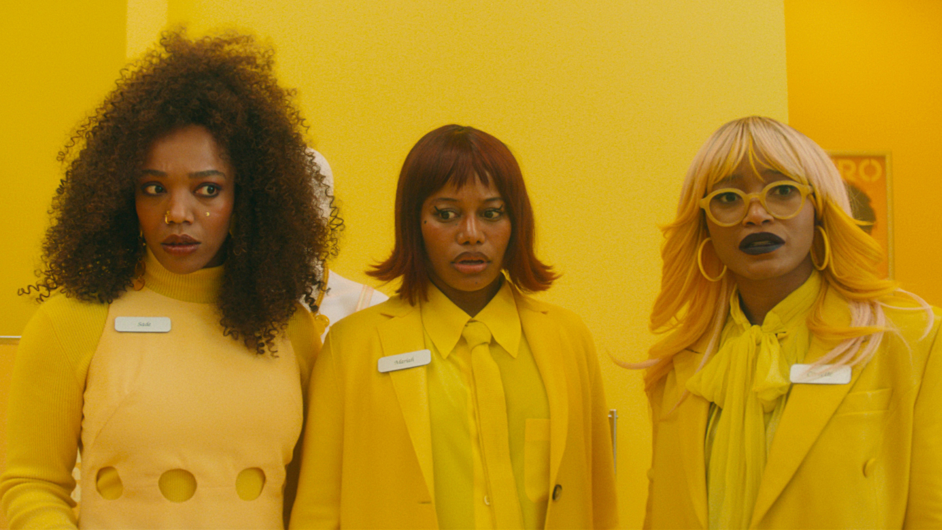 Three women (Naomi Ackie as Sade, Taylour Paige as Mariah, Keke Palmer as Corvette) look concerned while wearing all-yellow outfits and standing in a yellow store, in 'I Love Boosters'