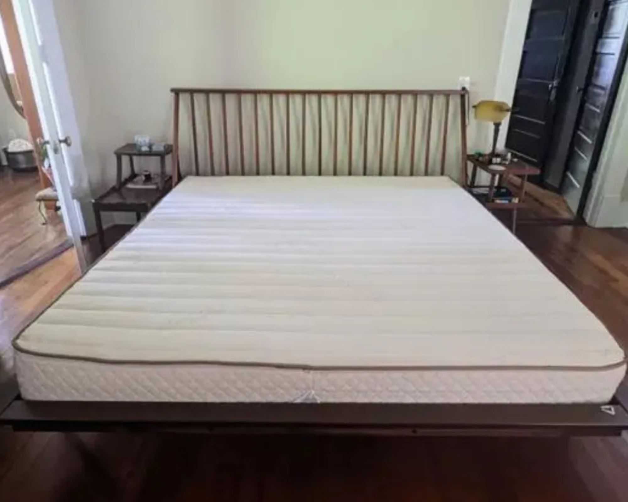 The PlushBeds Botanical Bliss Mattress seen on a wooden bedframe in a bedroom with wooden floors and white walls.
