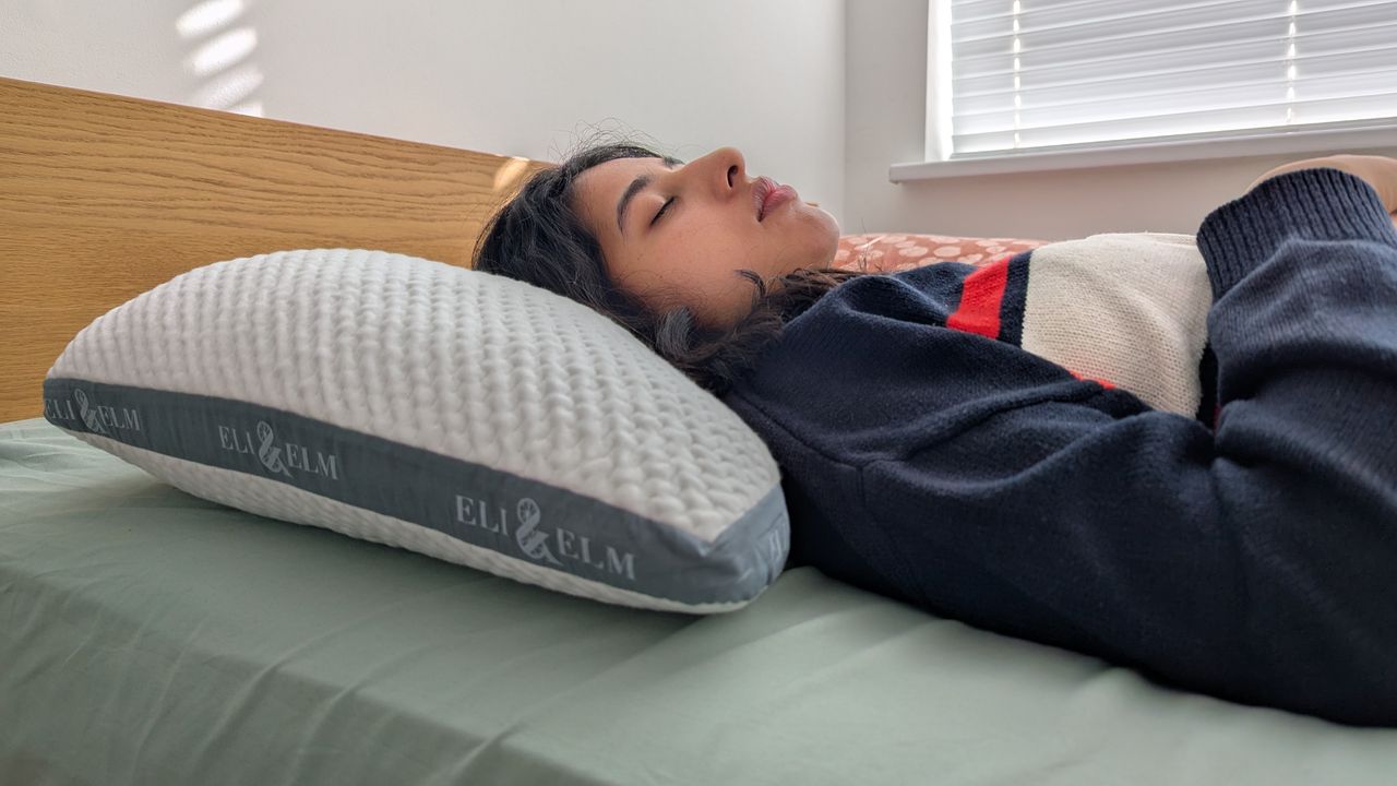 Woman sleeping on the Eli and Elm Side Sleeper Pillow in a bright lit room on the bed with a green bedsheet