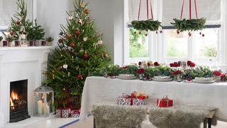 Dining room at Christmas time with decorated tree and dining table with natural foliage Christmas centerpiece that includes wreaths suspended above