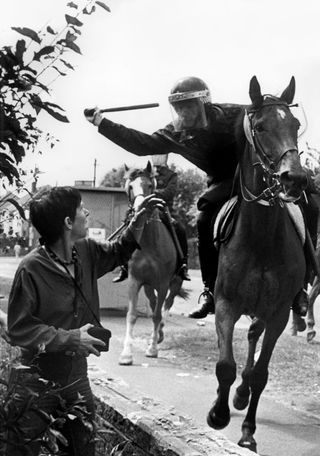 A mounted police officer hits a person with a baton