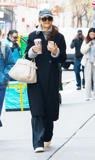 Katie Holmes wearing coat, gray sweater, pants, and baseball cap