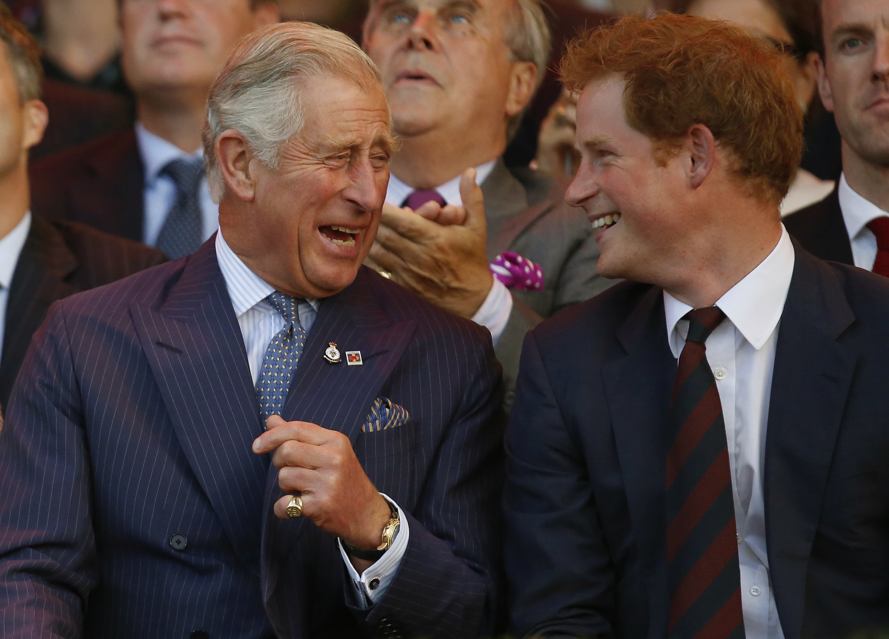 King Charles and Prince Harry sitting next to each other and laughing in blue suits