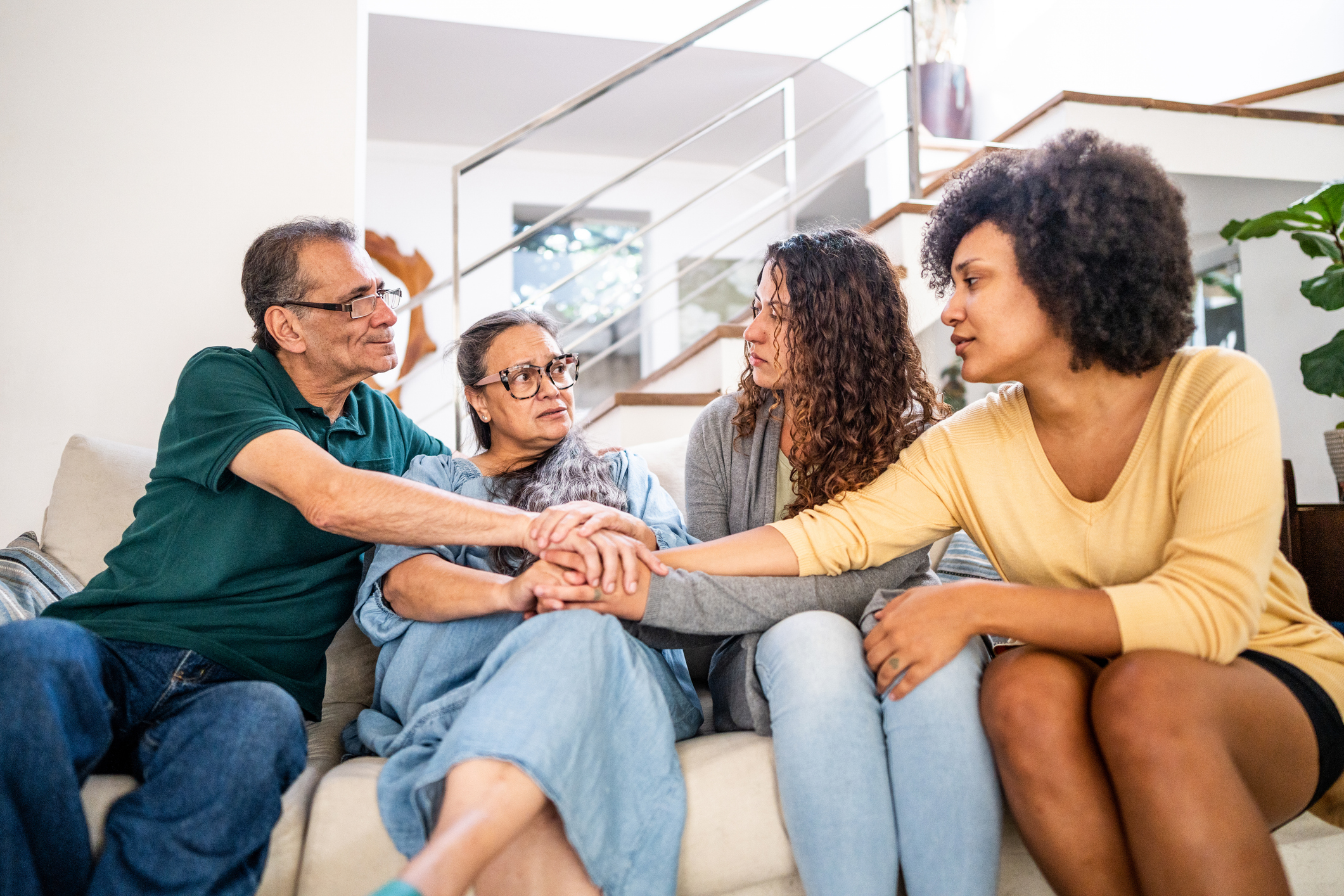 Young woman with her wife being comforted by her parents sitting on sofa in the living room at home