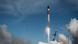a black and white rocket lifts off under a sunny blue sky