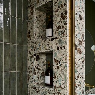 detail of a shower area with dark green tiles and a terrazzo wall with recessed cubby shelves for toiletries