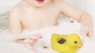 image of a baby playing with a yellow duck thermometer in foam bath as part of best baby bath products list