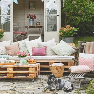 garden with pink and green colour scheme, pallet furniture, lounger, shed in background, dog, planters, lawn