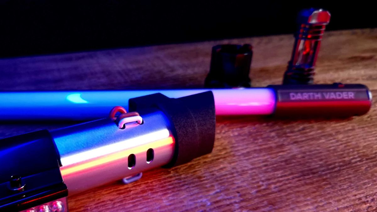 Darth Vader Force FX Elite Lightsaber hilt, blade, kyber crystal, and screw device on a wooden table in a darkened space