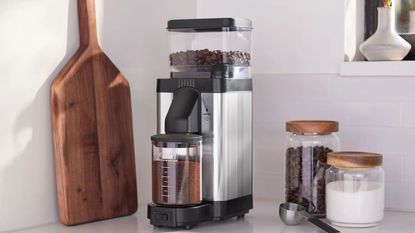 Moccamaster KM5 Burr Grinder on a countertop with a wooden chopping board, sugar, and coffee beans around it
