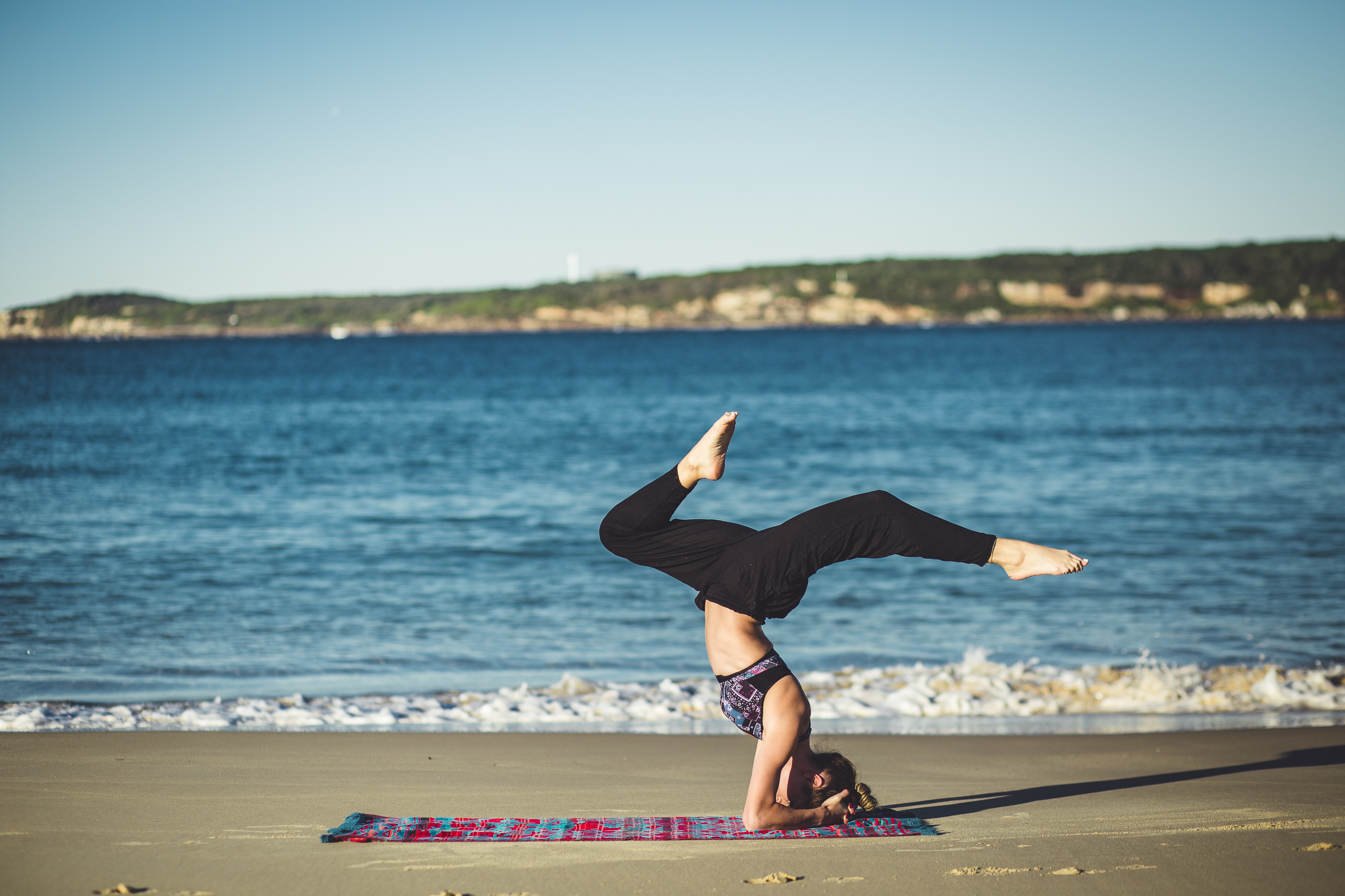 A woman poses on an exercise mat next to the ocean. 
