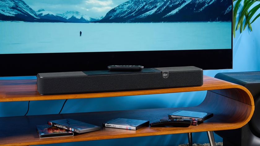 the klipsch flexus core 100 soundbar photographed on a wooden tv stand with a tv behind, showing the remote, buttons, and inputs