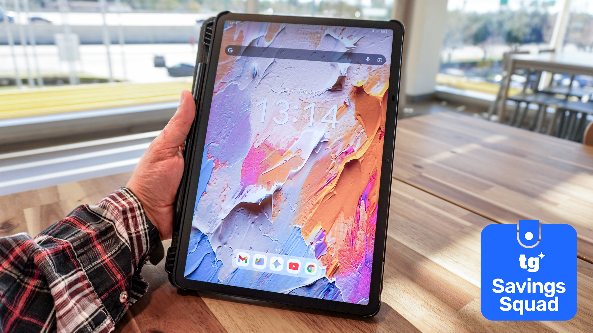 A person holding a TCL NXTPAPER 11 Plus tablet at a table with a Tom's Guide Savings Squad deals badge
