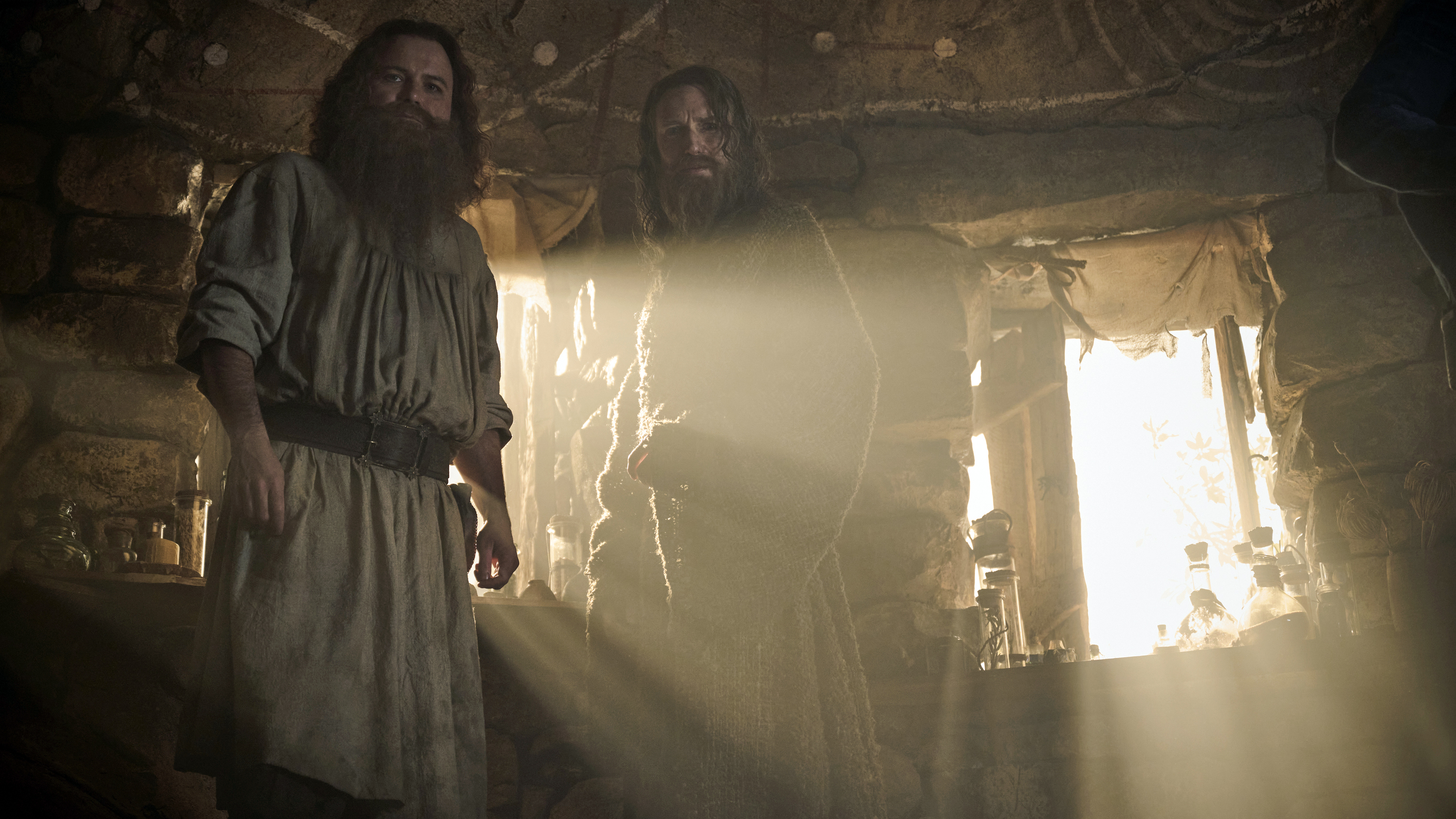 Tom Bombadil and The Stranger bathe in sunlight shining through a cabin window in Season 2 of The Rings of Power