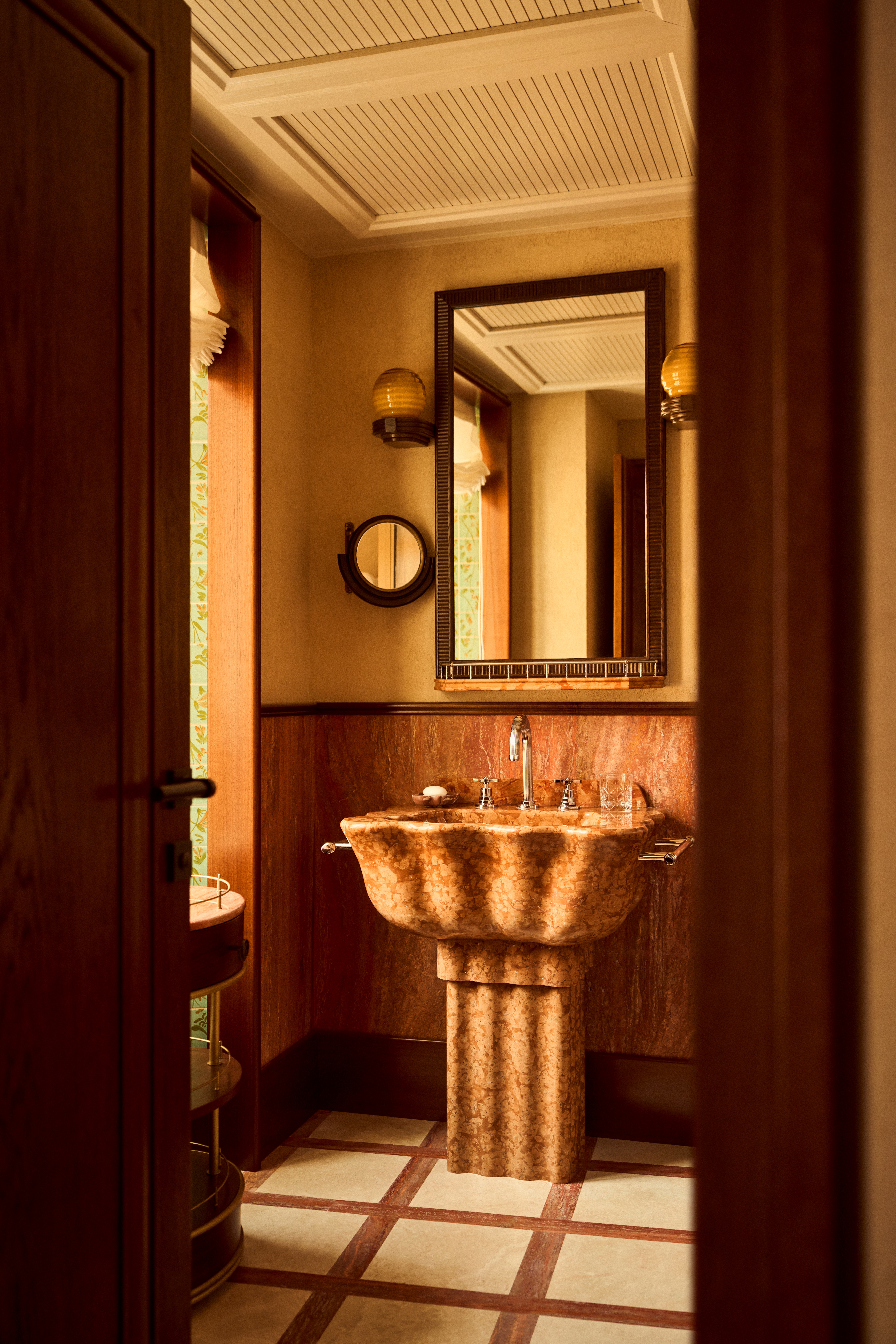 The interiors of a palatial hotel housed inside a 16th-century building with frescoed walls, textural arches, mesmerizing flooring, and plenty of wood oozes antique-inspired furniture and a golden atmosphere across sculptural furnishings, artworks, and plants.