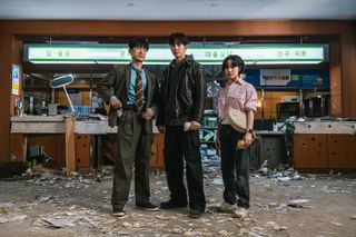 Three people pose in front of a trashed with bullet holes in the cabinets, in 'Cashero.'