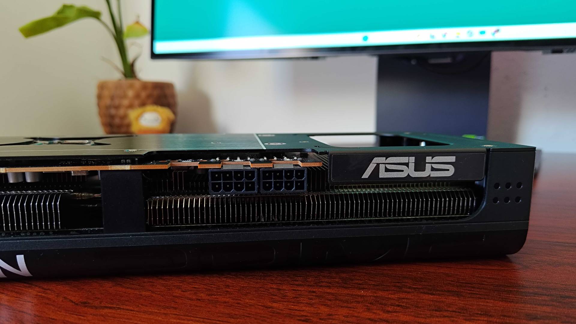 Close up of AMD Radeon RX 9070 Asus Prime graphics card logo and power connectors on woodgrain desk.