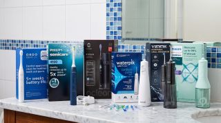 Selection of water flossers and electric toothbrushes arranged in a typical bathroom setting. 