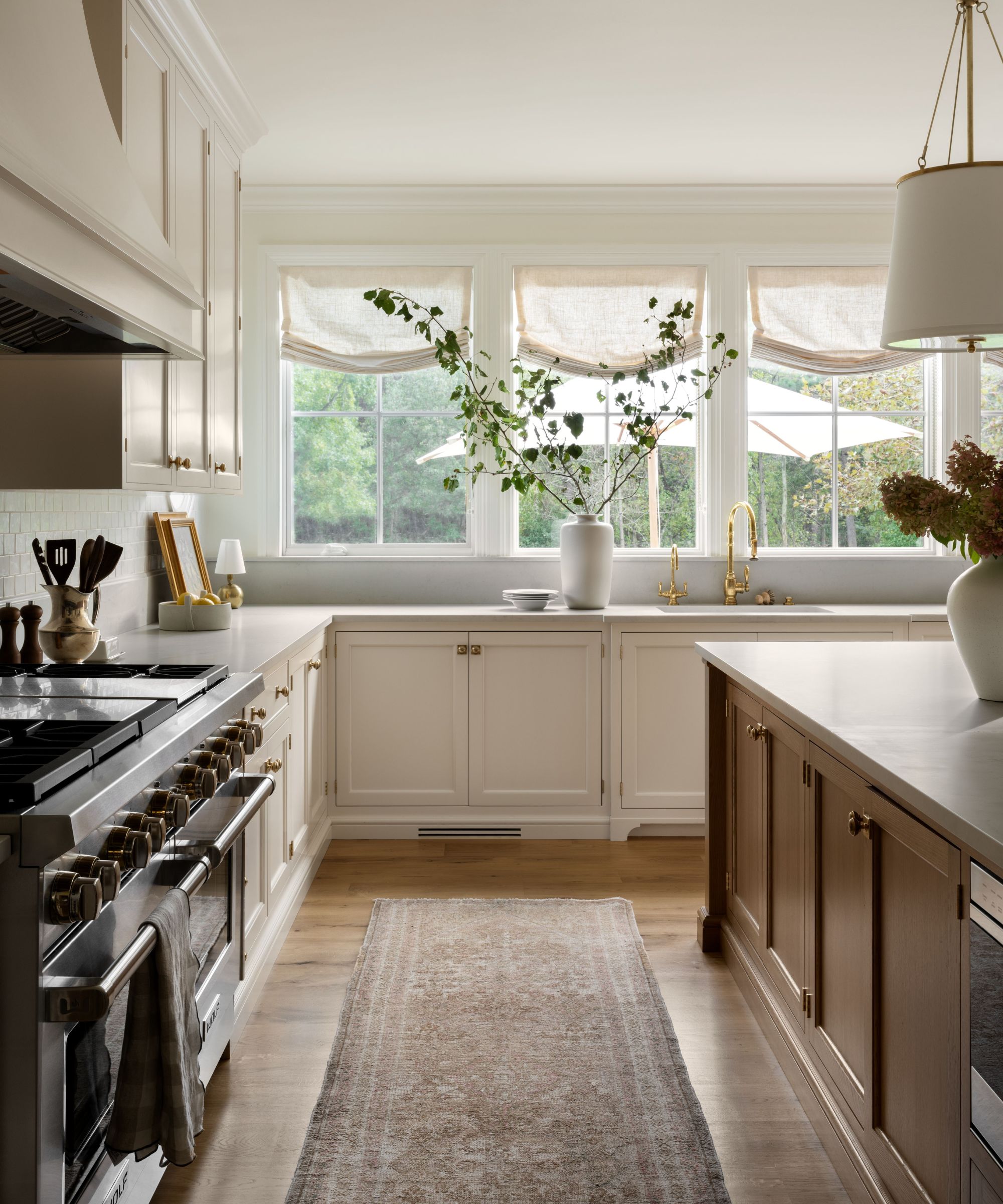 A warm neutral kitchen with off-white cabinets, gray countertops, a wooden island, and sheer linen fabric blinds over the windows
