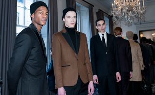 Featuring three models, A single, sharp black and white bow tie suit stood out among the more relaxed silhouettes that paired relaxed turtlenecks under tailored blazers, combined with long tweed coats, often worn closed with a knotted waist tie.