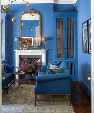 Azure blue painted living room with matching twin sofas, white fireplace, metallic mirror and pendant light