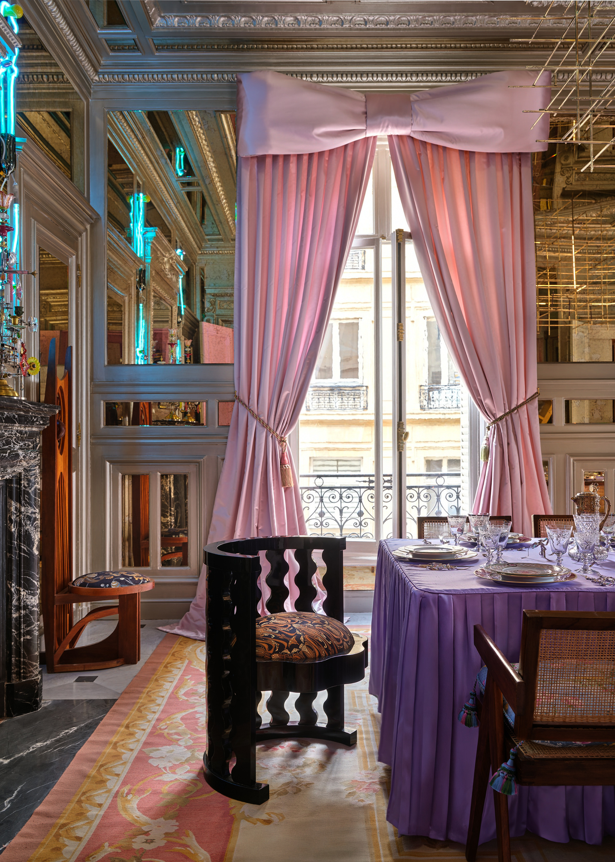 A high-ceilinged modern home with giant pink satin curtains framed with a bow on top and a purple table cloth on a dining table set for hosting