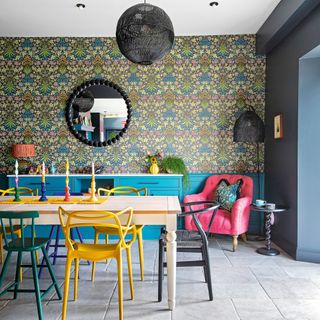 dining table with chairs in front of pink armchair and patterned wallpaper