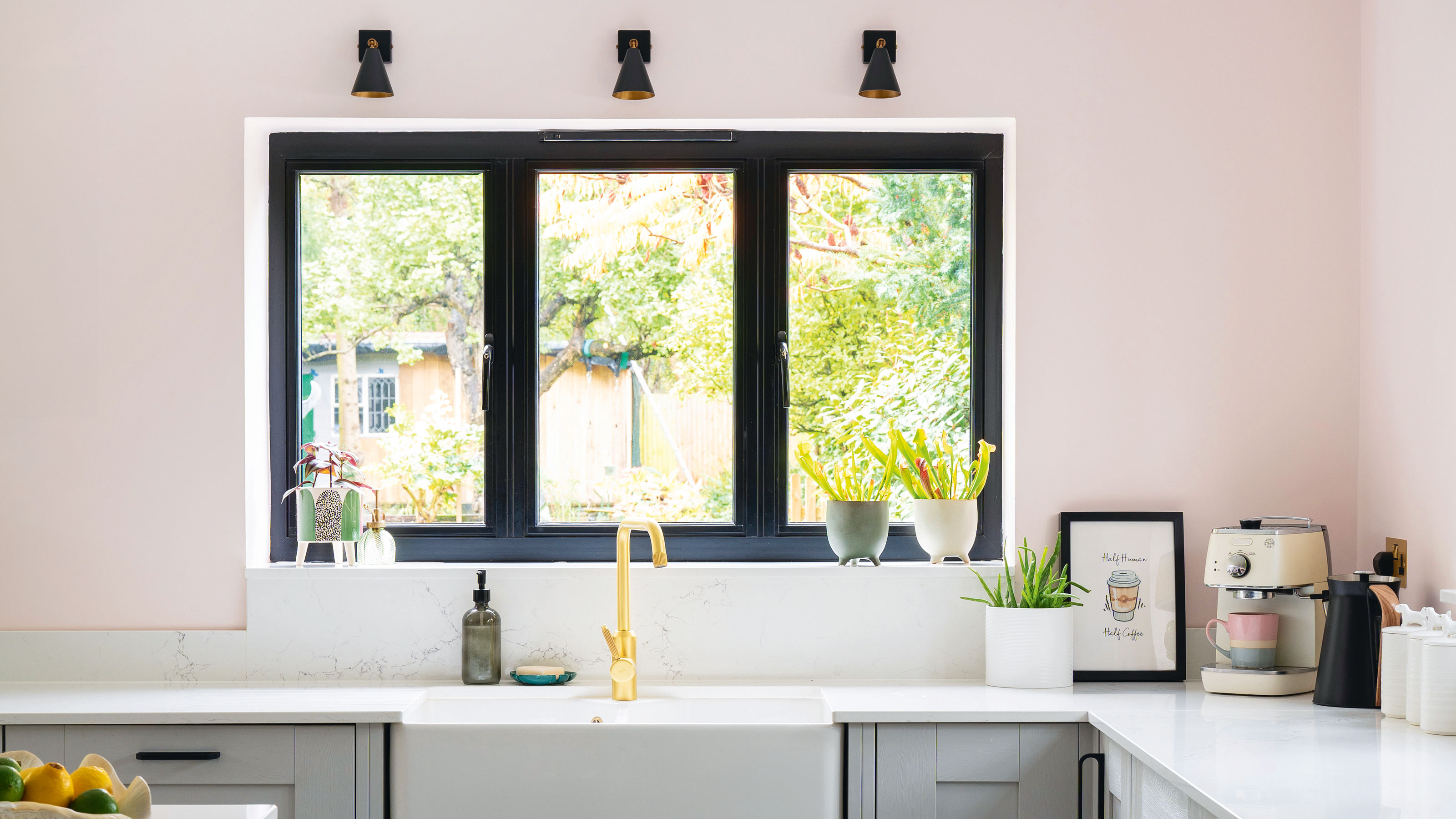 Pink walls and white kitchen worktop with grey cabinets and a kitchen sink under a window