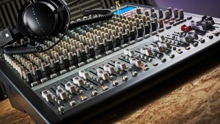 An audio mixer on a desk with a pair of headphones resting on top of it