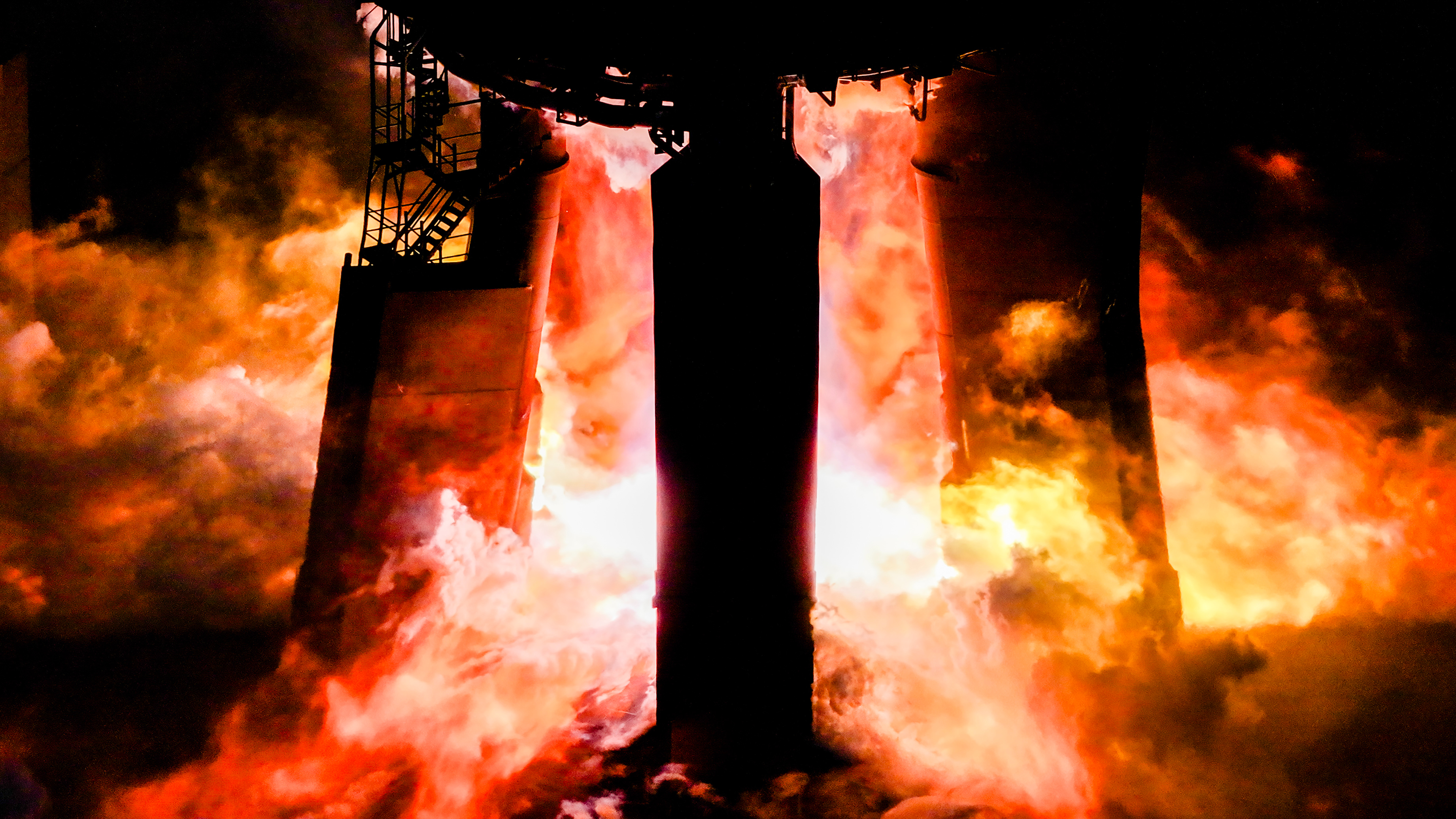 closeup of the base of a test stand where a rocket is being fired, with flames licking the stand's legs