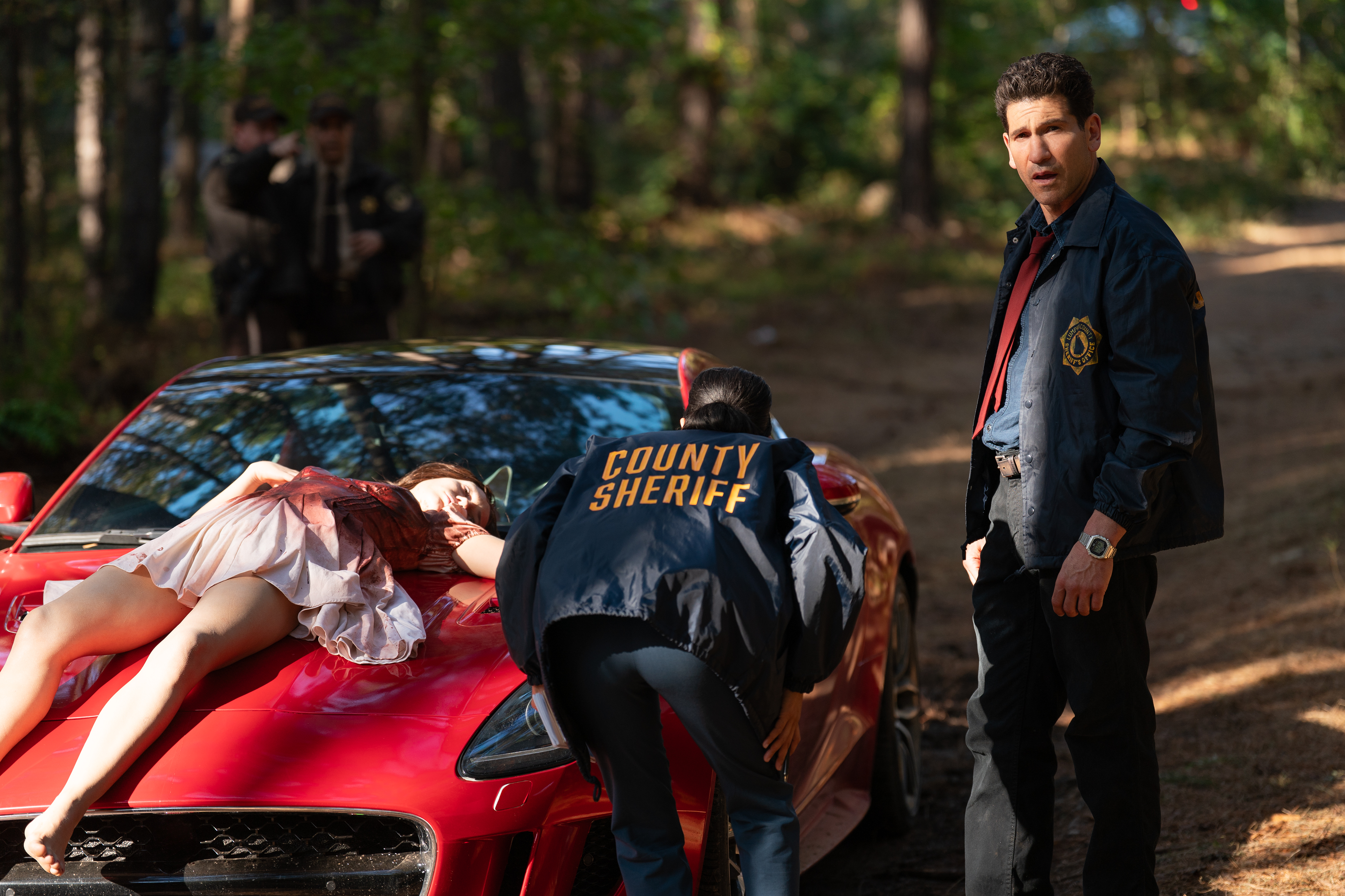 Sunita Mani as Priya and Jon Bernthal as Detective Jack Harper as they discover rachel's body stabbed to death on the hood of a car in the woods in the netflix miniseries his and hers