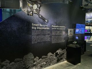 photo of an asteroid exhibit at a space museum, showing a glass display case and a dark wall with text on it.