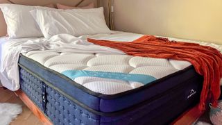 Review image shows the a white mattress cover pulled back on the DreamCloud Premier Hybrid mattress, which is dressed with a burnt-orange throw