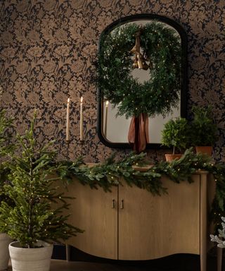 christmas garland on cabinet with wreath displayed on mirror and small potted christmas tree