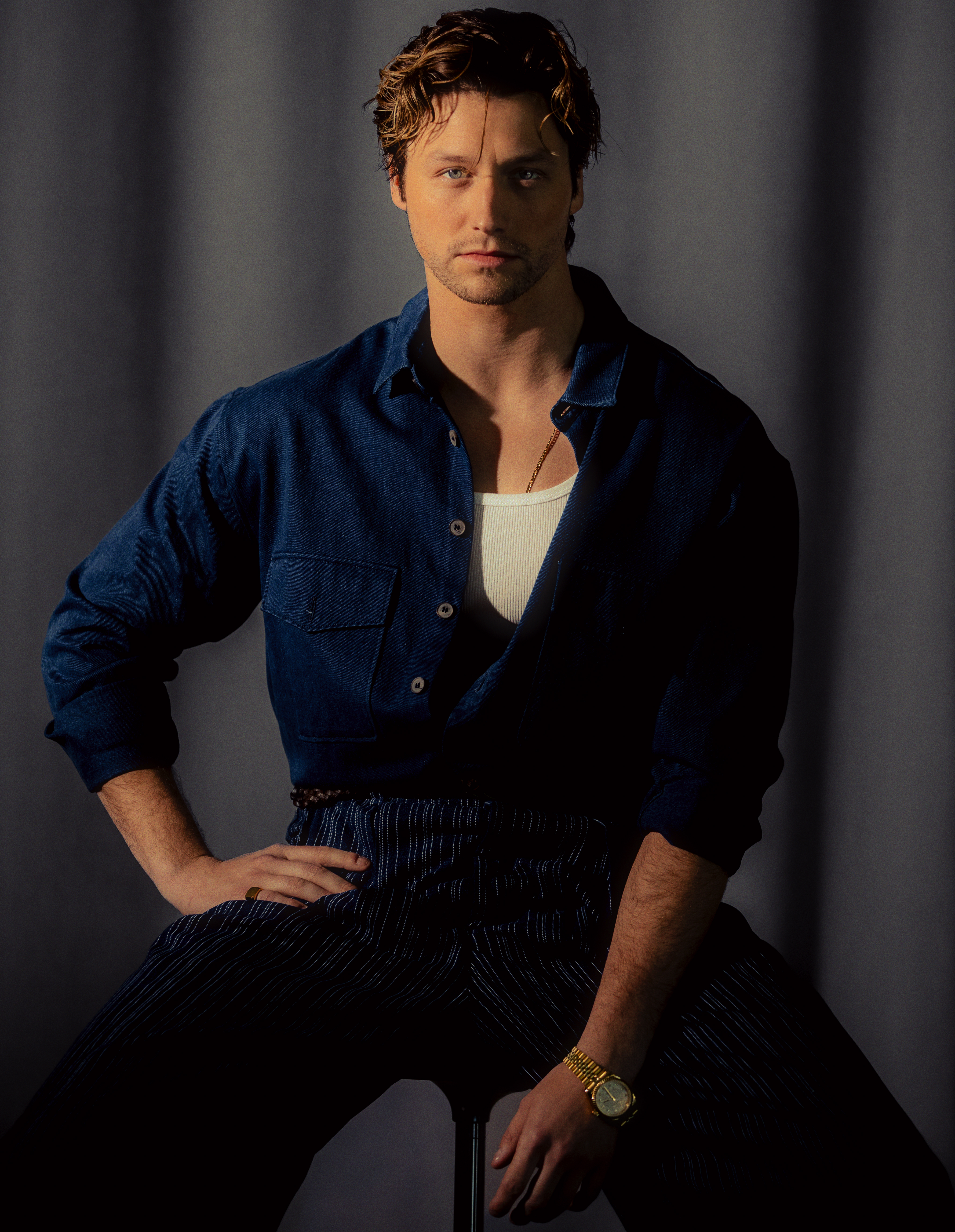 Off Campus star Stephen Kalyn wearing a blue button-down, a white tank underneath, and navy pants.