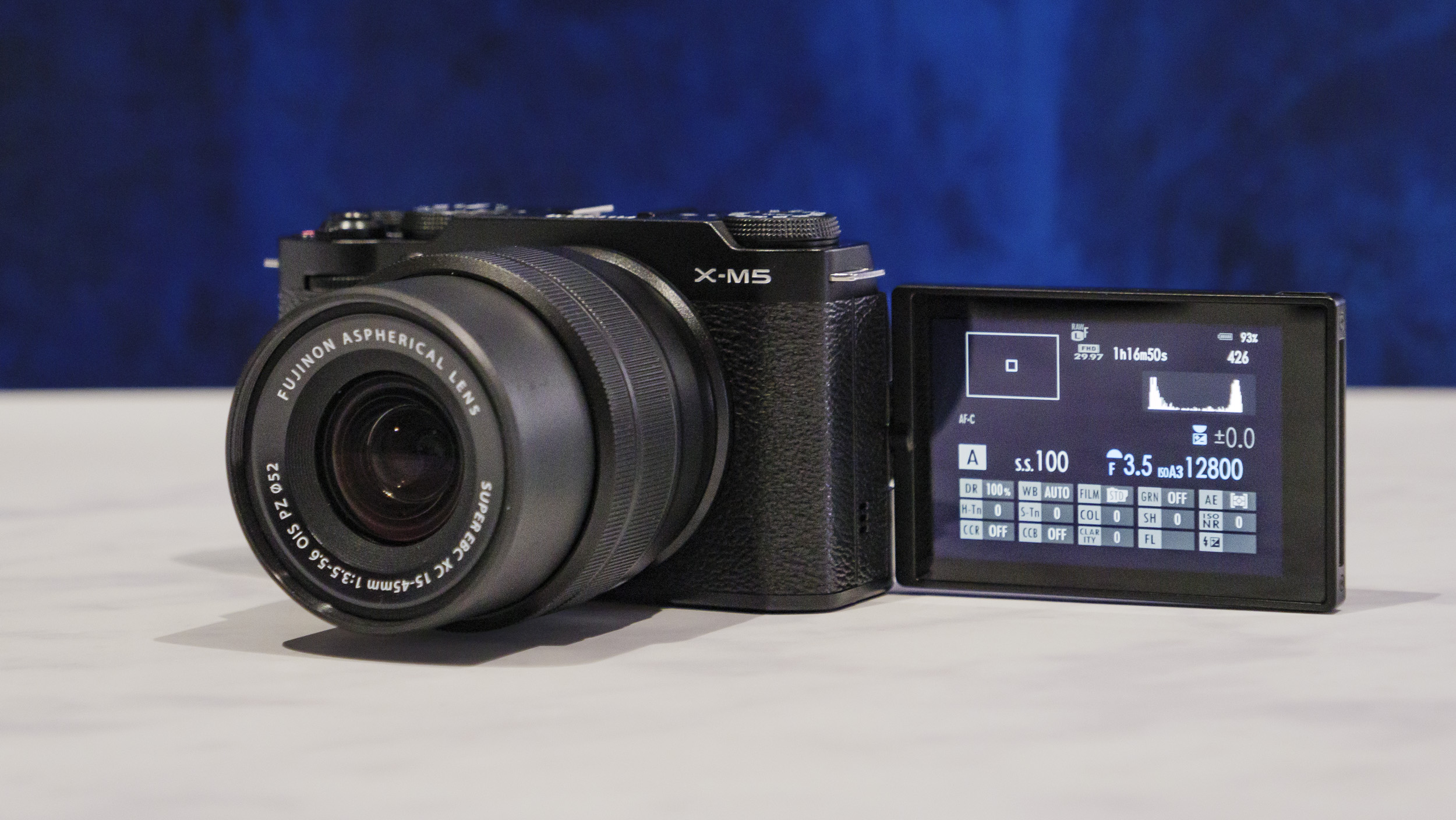 Fujifilm X-M5 camera  with flip screen out, on a marble surface with rich blue background