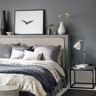 Grey bedroom with headboard shelf and bed layered with cushions and throws