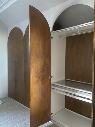 A large closet with open wooden arched doors and sliding pull out shelves