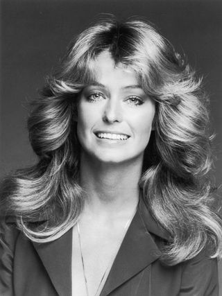 Studio headshot portrait of American actor Farrah Fawcett smiling while wearing a dark blouse and a chain.