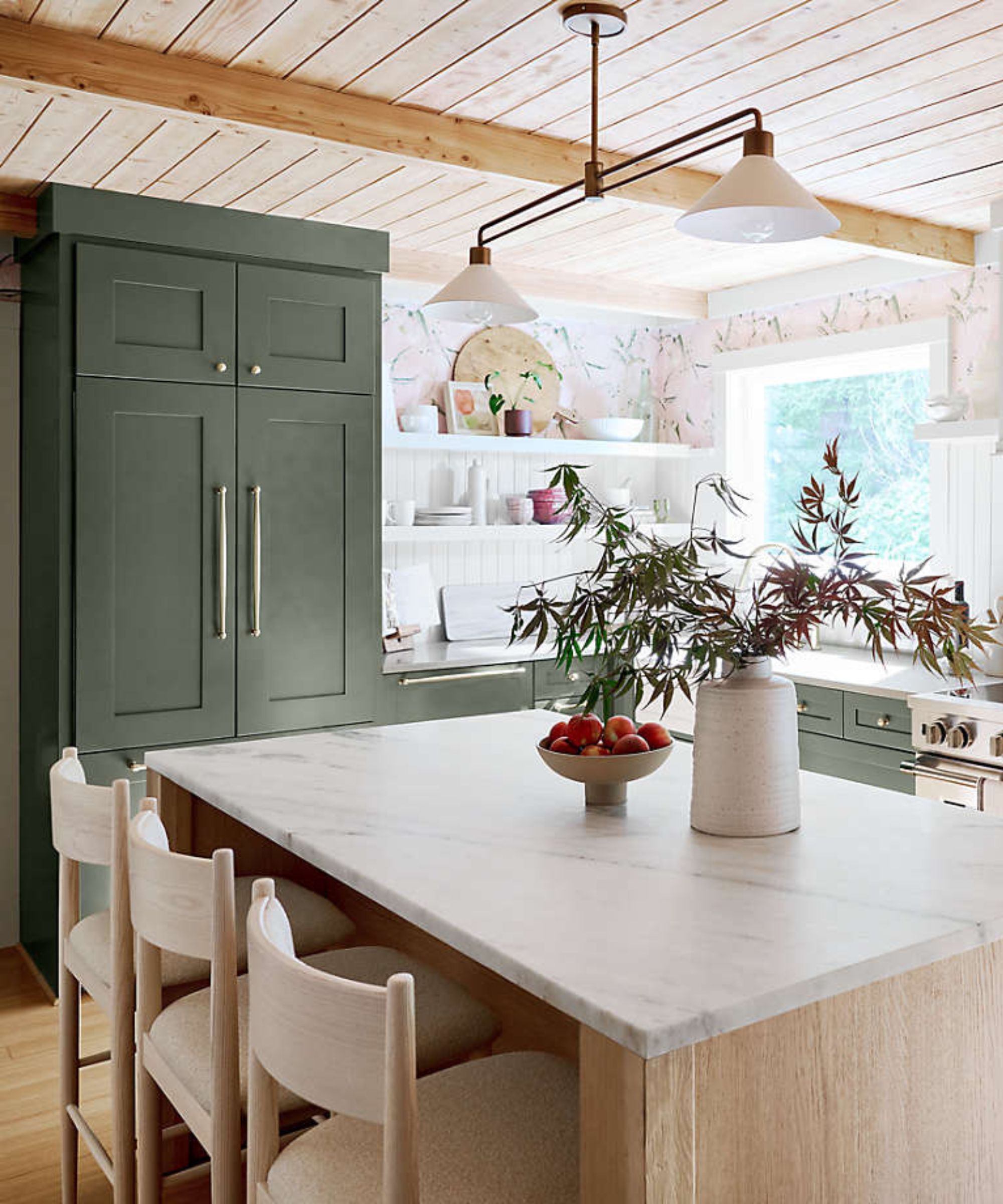 A kitchen with paneled white walls, green cabinetry, and wooden island, marble countertops, and brass hardware