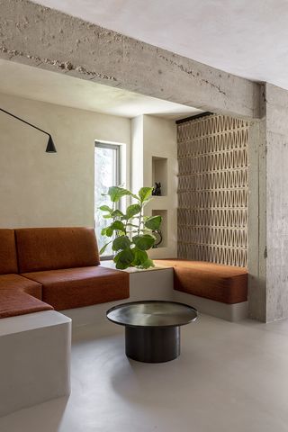 orange corner sofa in brutalist design living space with unshaven cement beams