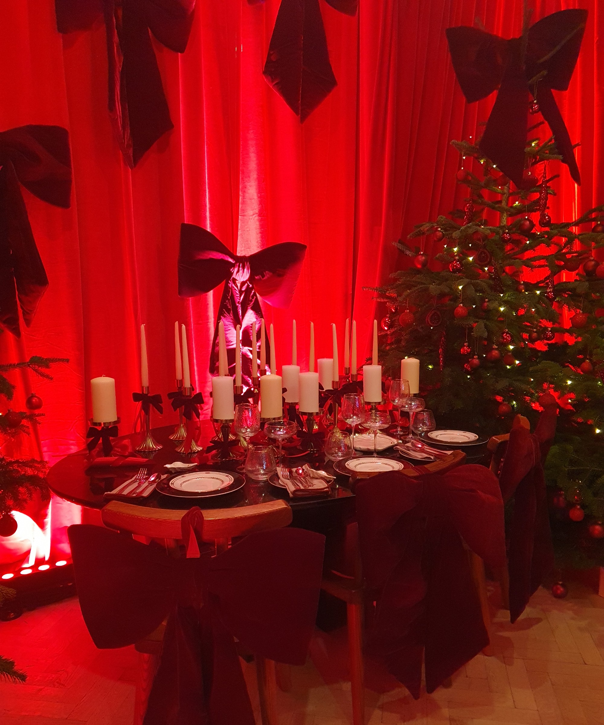 XXL red velvet Christmas bows at thee M&amp;amp;S press show adorning backs of chairs, the Christmas tree and a curtain-covered wall