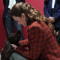 Princess Kate wearing an orange coat petting a black dog 