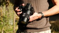 Person holding the Sony RX10 V with both hands outdoors in bright sunlight.
