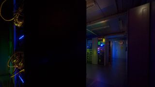 A dark room light up by blue light showing a series of servers and wires