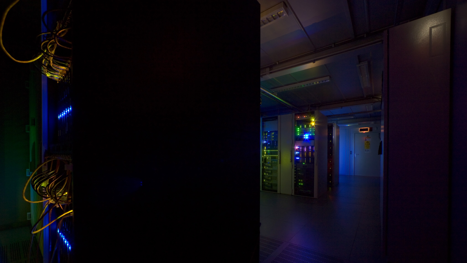 A dark room light up by blue light showing a series of servers and wires
